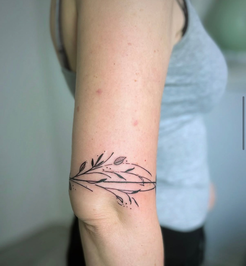 Fine line botanical branch tattoo wrapping the upper arm